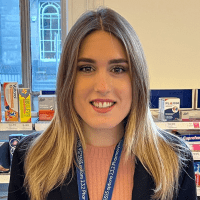 A woman with blonde/brown hair smiles at the camera from behidn the pharmacy counter